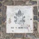Atentát na papeže Jana Pavla II. 1981 - Místo střelby je označeno malou mramorovou dlaždicí s osobním erbem Jana Pavla II. a datem římskými číslicem – wikipedia .